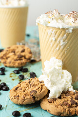 Close-up of two cardboard cups with coffee and cream, selective focus, on blue table with cookies with cream and coffee beans, vertical