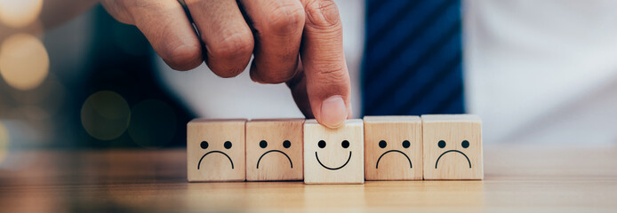 Satisfaction concept, Close up customer hand choose smiley face and blurred sad face on wood cube, banner cover design.