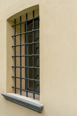 Vintage black metal wrought iron grille on the window of a rough wall with yellow plaster. Vertical orientation, selective focus, side view, copy space