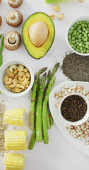 Vertical image of high angle of fresh avocado, beans, mushrooms, corn and asparagus on white
