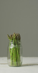 Vertical image of fresh stalks of asparagus in glass jar on grey background