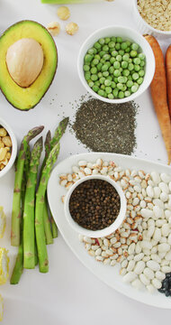 Vertical image of high angle of fresh avocado, beans, mushrooms, corn and asparagus on white