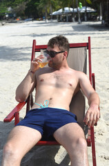 Young man drinking beer and sitting on deck chair at beach in Nha Trang
