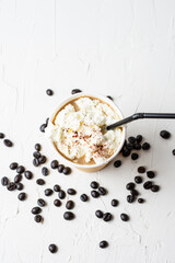 Top view of cardboard cup with coffee with cream, cocoa and black straw, on white table with coffee beans, selective focus, vertical