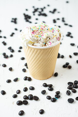 Fototapeta na wymiar Top view of cardboard cup with coffee with cream and colored toppings, on white table with coffee beans, selective focus, vertical