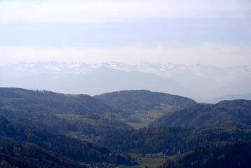 Fototapeta premium Aerial view over rural landscape with Swiss Alps in the background seen from local mountain Uetliberg on a blue cloudy spring day. Photo taken April 21st, 2022, Zurich, Switzerland.
