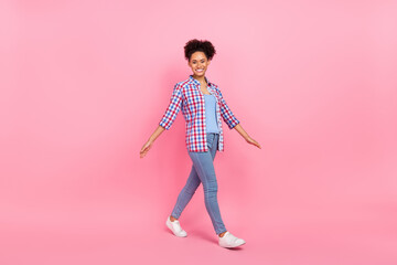Full length body size view of attractive cheerful wavy-haired girl going wearing checked shirt isolated over pink pastel color background