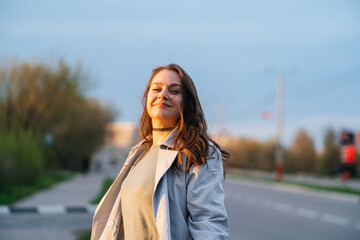 Fototapeta premium beautiful smiling girl with long hair in a grey trench coat outdoors on the street spring