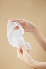 Front view of hand holding a mask in beige background for cosmetic advertising