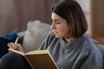 stress, mental health and depression concept - sad crying woman with diary sitting on sofa at home