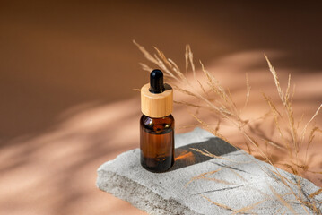 Amber glass dropper with bamboo lid and dry plant. Bottle on grey concrete podium for product...