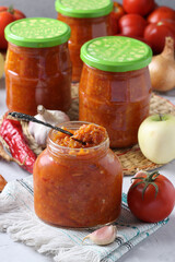 Homemade caviar from apples, carrots, peppers, garlic and tomatoes in glass jars on light gray background