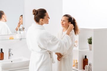 beauty, hygiene, morning and people concept - happy smiling mother cleaning daughter's ear with cotton swab in bathroom