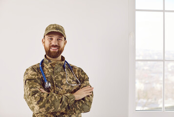 Happy army doctor inside hospital. Man with ginger beard in camouflage uniform with stethoscope...
