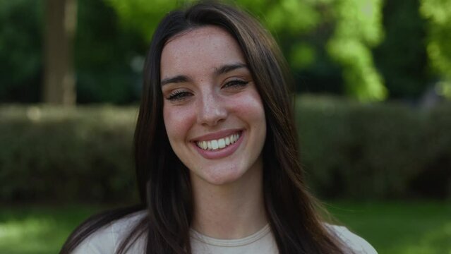 Beautiful happy young caucasian woman smiling at camera standing outdoors. Positive millennial female portrait in city park - High quality 4k footage