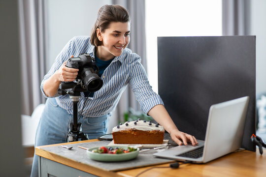 blogging, profession and people concept - happy smiling female food photographer with laptop computer and camera photographing cake in kitchen at home