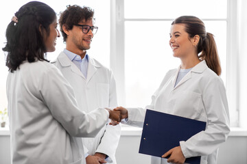 science, work and people concept - international group of happy scientists shaking hands in laboratory