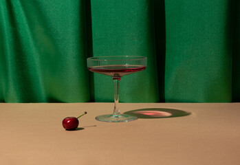 Champagne glass, cherry, rich green drapery. Creative fruity cocktail arrangement. 60s vibes.  - obrazy, fototapety, plakaty