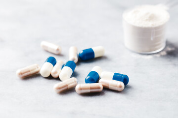 Sport supplements (carnitine and creatine capsules) and Scoop of whey protein on bright stone background. Soft focus. Close up.
