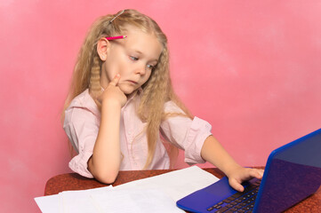little schoolgirl is typing on a laptop at the table. pink background.