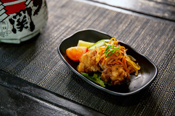 Nanbanzuke karaage chicken in the traditional Japanese ramen restaurant, with a black plate on a black mat and Japanese fonts sake barrel translation: Invincible Great Gate