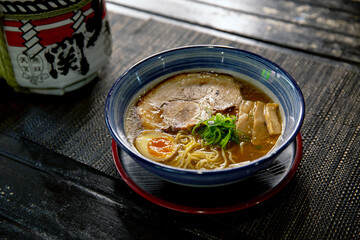 Pork tonkotsu chashu ramen in the traditional Japanese ramen restaurant, with a black plate on a ramen bowl and Japanese fonts sake barrel translation: Invincible Great Gate