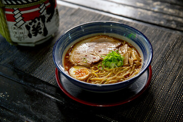 Spicy pork tonkotsu chashu ramen in the traditional Japanese ramen restaurant, with a ramen bowl on a black mat and Japanese fonts sake barrel translation: Invincible Great Gate