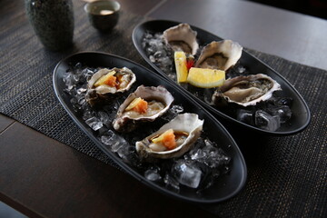 Fresh oysters appetizer with sauce and lemons in the traditional Japanese ramen restaurant, with a black plate on a black mat in a black scene background