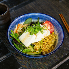 Veggie tofu cold ramen with salad in the traditional Japanese ramen restaurant, with a ramen bowl on a black mat