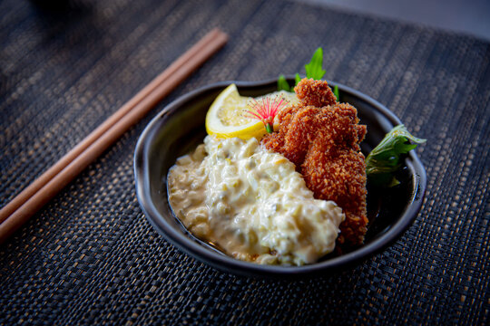 Nanban Chicken Katsu fried chicken appetizer in the traditional Japanese ramen restaurant, with a black plate on a black mat in a black scene background