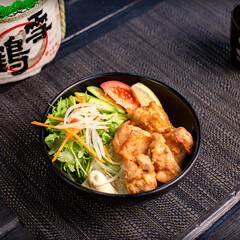 Fried chicken karaage don with salad in the traditional Japanese ramen restaurant, with a black bowl on a black mat and Japanese fonts sake barrel translation: Snow Crane