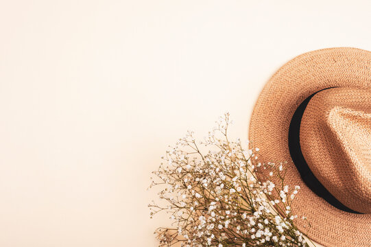 Female summer straw hat and gypsophila plant on neutral beige background. Top view, flat lay, copy space