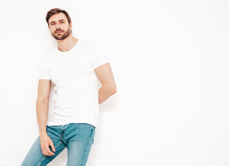 Fototapeta premium Portrait of handsome smiling stylish hipster lambersexual model. Sexy man dressed in T-shirt and jeans. Fashion male isolated on white wall in studio