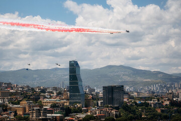 Independence Day of Georgia. Airplanes are flying over Tbilisi and making colored smoke. Helicopters carry the national flag - 507060352