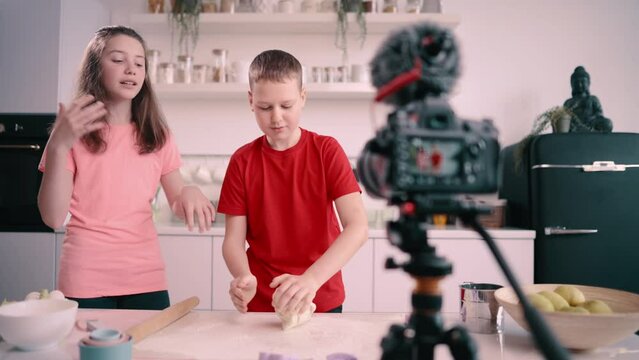Boy and girl recording culinary blog at home. Boy kneading dough on table.