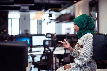 Multiethnic startup business team Arabian woman wearing a hijab on meeting in modern open plan office interior brainstorming, working on laptop and desktop computer. Selective focus 