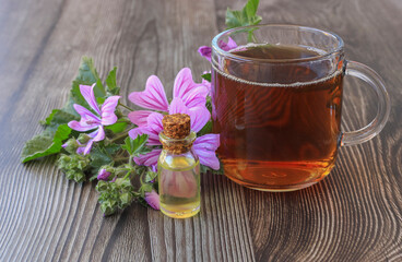 Hibiscus tea and hibiscus flowers in a glass cup on a wooden table. Vitamin tea for cold and flu and hibiscus oil in bottle