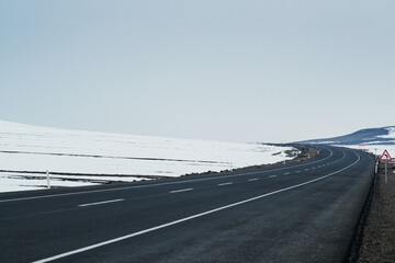 Fototapeta premium Diagonal view of an emtpy asphalt and bending road with lanes and snow in winter