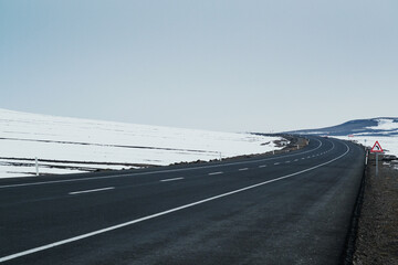 Diagonal view of an emtpy asphalt and bending road with lanes and snow in winter