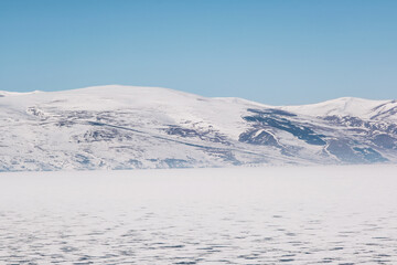 Landscape view of Frozen Cildir lake in Kars and snowy mountains with a blue sky in winter