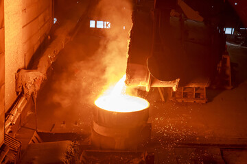 Hot steel pouring from big casting ladle into a mold in an iron foundry.