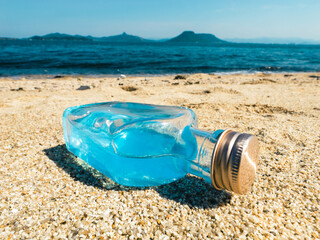 A glass bottle of blue water on the beach on sunny day, Tropical summer vacation background	