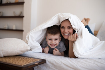 Happy family mom and son lying under blanket in bed at home. mom with child have fun in bedroom.