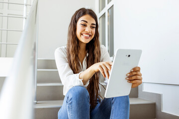 Smiling young woman using tablet computer isolated on white office background . Young female college student using tablet on a staircase. Attractive young woman using a digital tablet