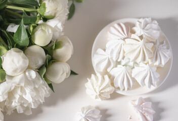 Fototapeta na wymiar Bouquet of white peonies on a white background and white meringue cookies.