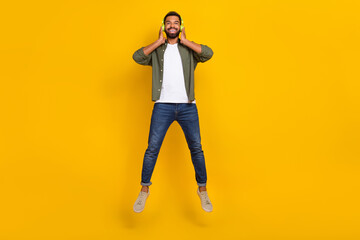 Fototapeta na wymiar Full length photo of dreamy positive guy dressed green shirt hands headphones jumping high isolated yellow color background