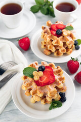Belgian waffles with strawberries on plates, tea cups and cutlery. Tea party concept.
