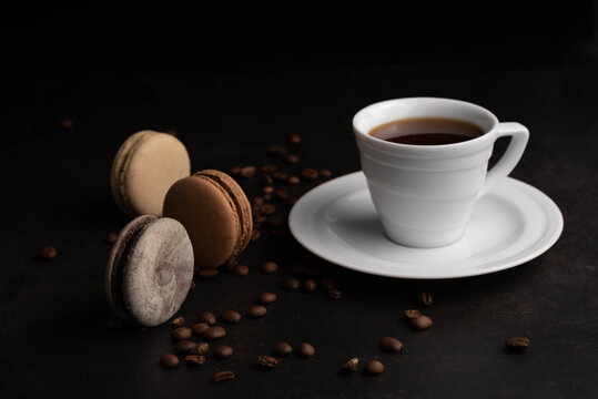 Blurred image of macaroons, coffee beans and a cup of espresso on a black background. Coffee drinking concept.