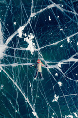 Woman tourist on ice skates and with long red scarf on frozen cracks lake Baikal, aerial top view