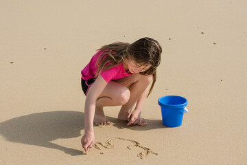 pretty young girl drawing in the sand with her finger